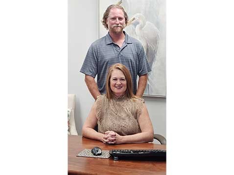 A woman sitting at a desk with a man behind posing for a photo