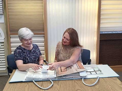 Two women sitting at a desk looking at fabric samples