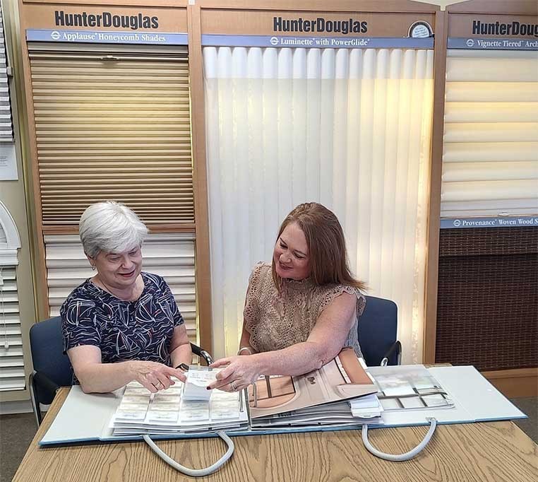Two women sitting at a desk looking at fabric samples